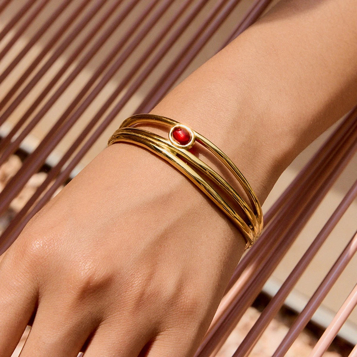 Gold bracelet with a red gemstone on a wrist against a blurred background