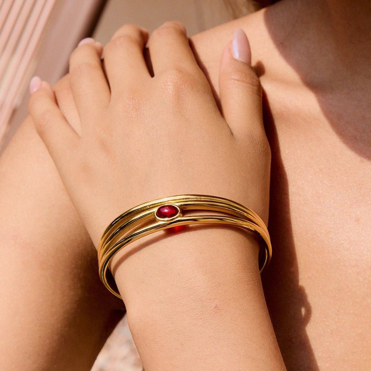 Gold bracelet with a red gemstone on a wrist against a neutral background