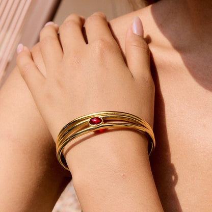 Gold bracelet with a red gemstone on a wrist against a neutral background