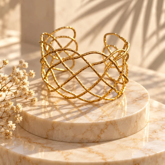 The Lattice Gold Open-Weave Wide Cuff Bangle on deep red velvet — close-up showing hammered gold wire texture across interlaced diamond-grid strands with glowing warm finish