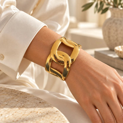The Interlock Gold Cuban Link Wide Open Cuff Bangle product shot on cream background — three-quarter view showing full sculptural Cuban link silhouette with open back and high-polish gold finish