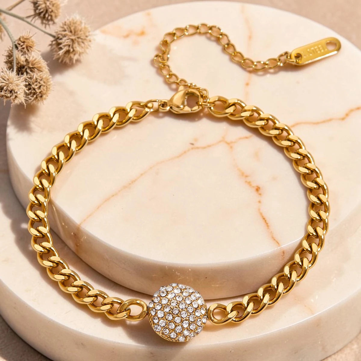 The Orbit Gold Pavé Crystal Ball Chain Bracelet — flat lay on cream textured surface showing gold Cuban link chain with empty ball setting detail