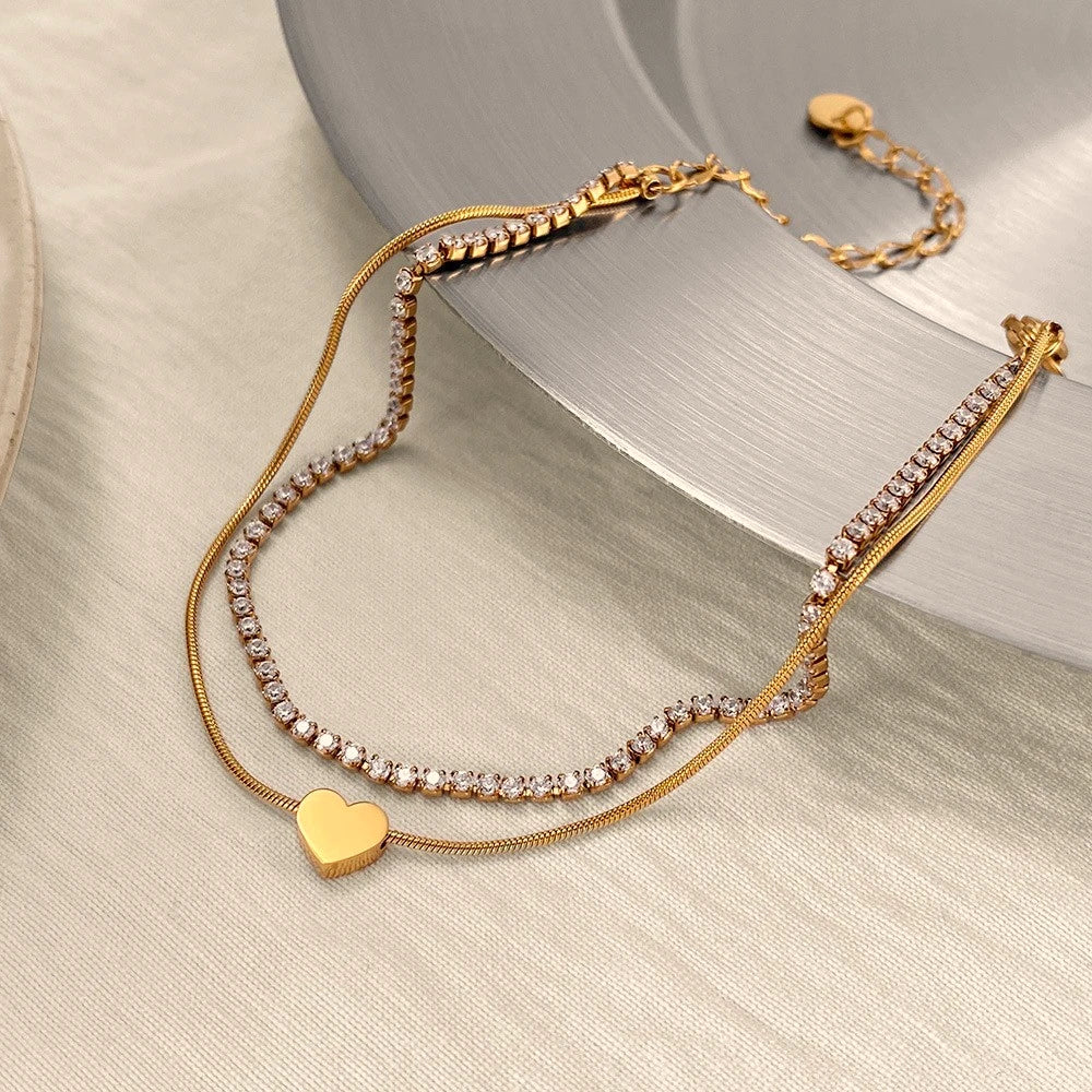 The Duo Gold Heart Charm Double Layer Bracelet — styled flat lay on marble tray with dried flowers showing full bracelet and lobster clasp detail
