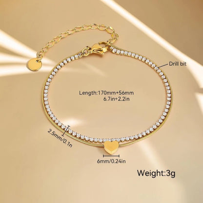 The Duo Gold Heart Charm Double Layer Bracelet — flat lay on peach surface with seashell prop showing tennis and snake chain layers
