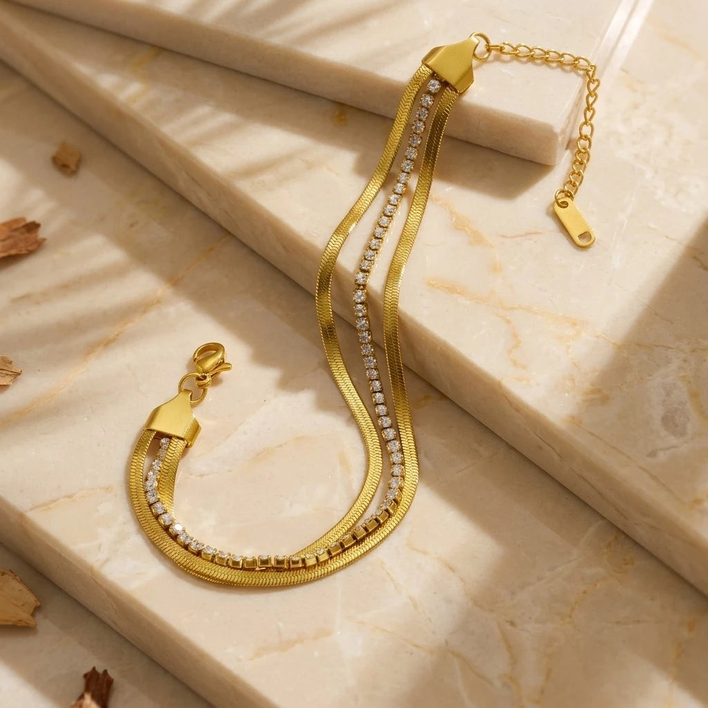 The Glide Gold Tennis & Herringbone Double Layer Bracelet — flat lay on cream jewellery box lid showing parallel herringbone and crystal tennis chains with shared gold end caps