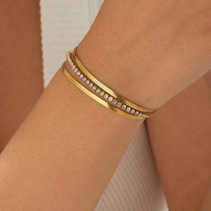The Glide Gold Tennis & Herringbone Double Layer Bracelet — flat lay on marble steps showing full length of both chain layers with lobster clasp and extender chain