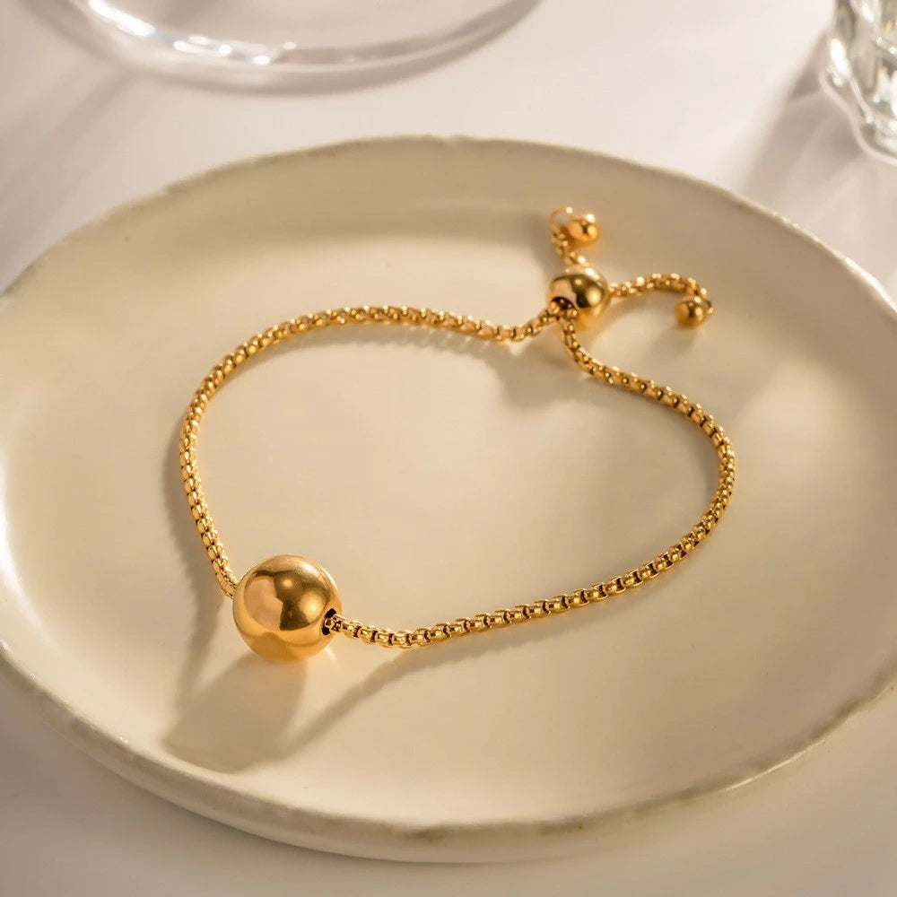The Orbit Gold Sphere Slider Bracelet — close-up on hand showing slider closure with two gold ball-tipped tails and how the box chain threads through the sliding bead
