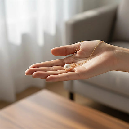 The Pearl Drop Single Pearl Pendant Necklace held in open hand indoors – showing scale of baroque freshwater pearl with decorative gold leaf bail on satellite chain